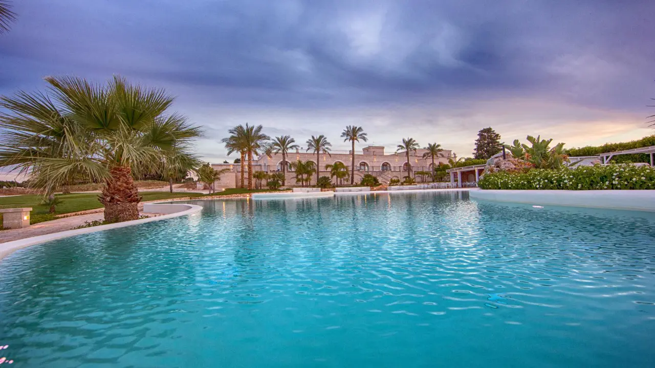 Scenic view of the outdoor pool at Masseria Caselli Hotel, Italy, surrounded by palm trees and gardens at sunset