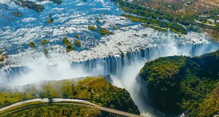 Aerial view of Victoria Falls in Zimbabwe, with water cascading over the cliffs and mist rising above the surrounding landscape