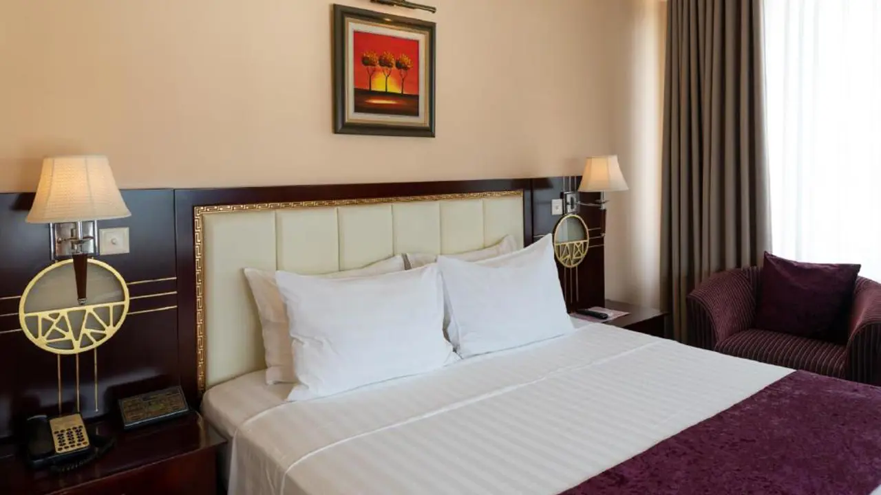 Elegant bedroom at Flower Garden Hanoi Hotel with warm wooden furniture, white linens, soft lighting, and traditional Vietnamese decor touches