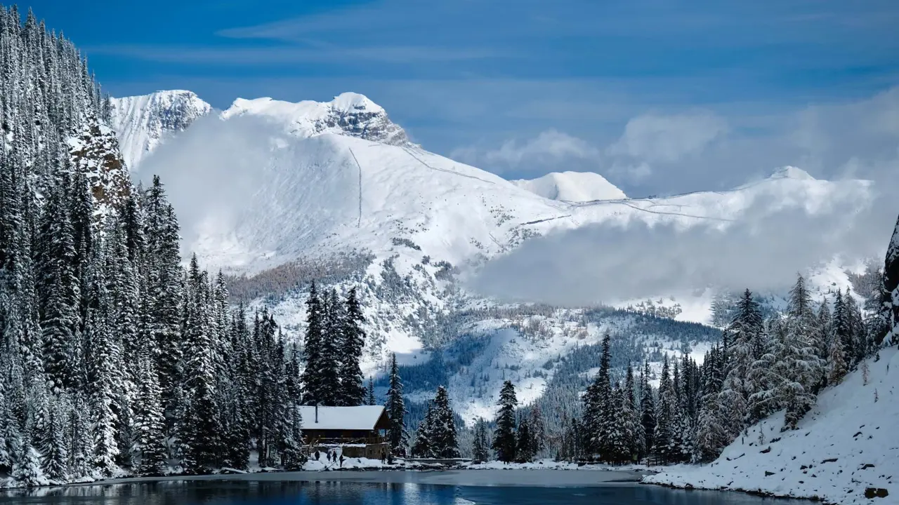 The Tea House at Lake Agnes nestled in snow-covered mountains beside a blue alpine lake