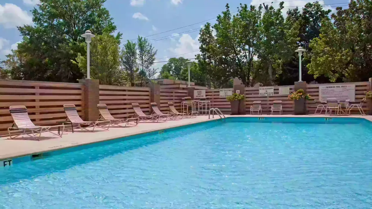 Outdoor swimming pool with loungers along the side, surrounded by a wooden fence and trees at the Holiday Inn Nashville Vanderbilt