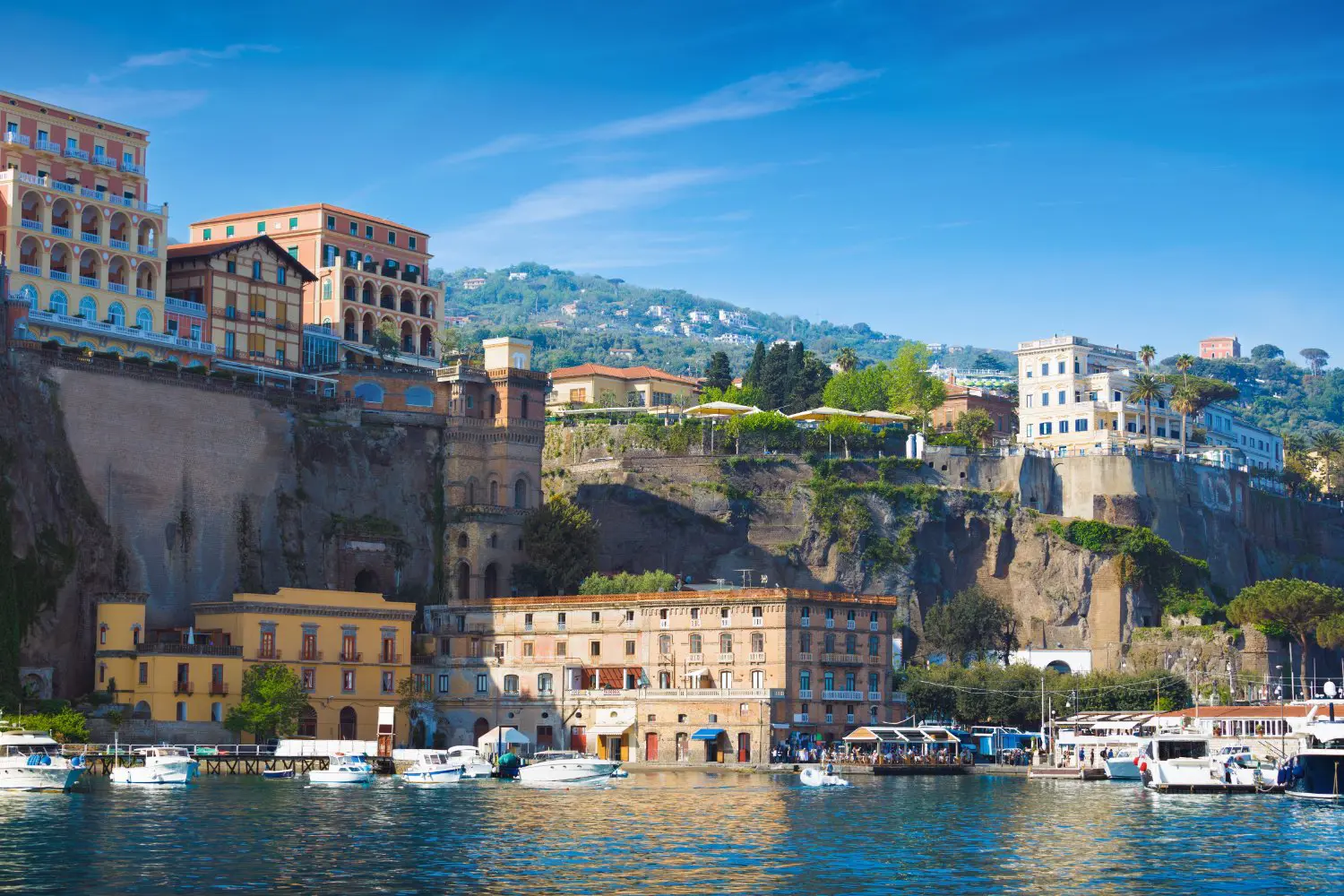 A sunny day in Sorrento, Italy, with multicoloured luxury hotels on the cliffs above a peaceful marina