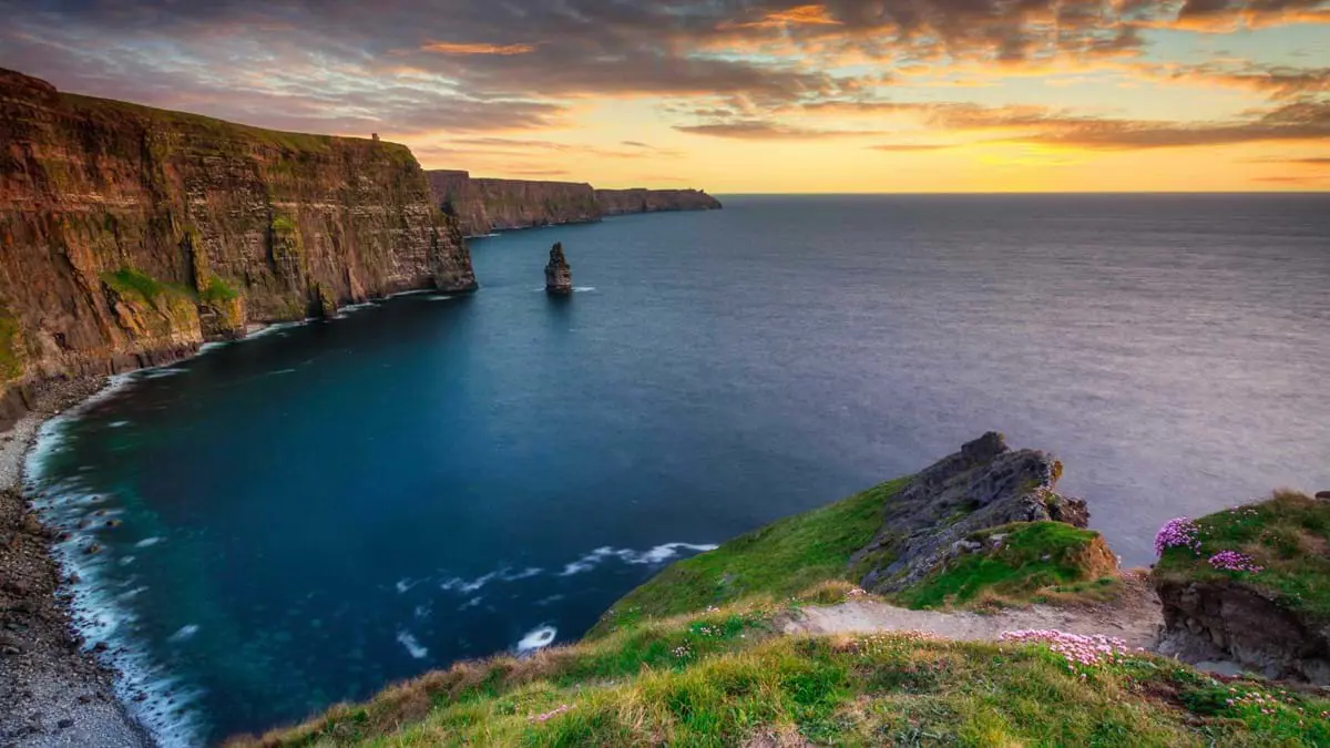 High angle shot of a coast line, with cliffs that curve to the right and rocky land in the right forefront 