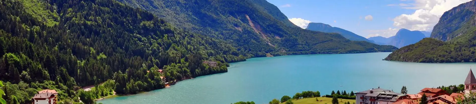 Molveno Lake in Italy, with colourful houses in the foreground and rolling hills alongside the lake