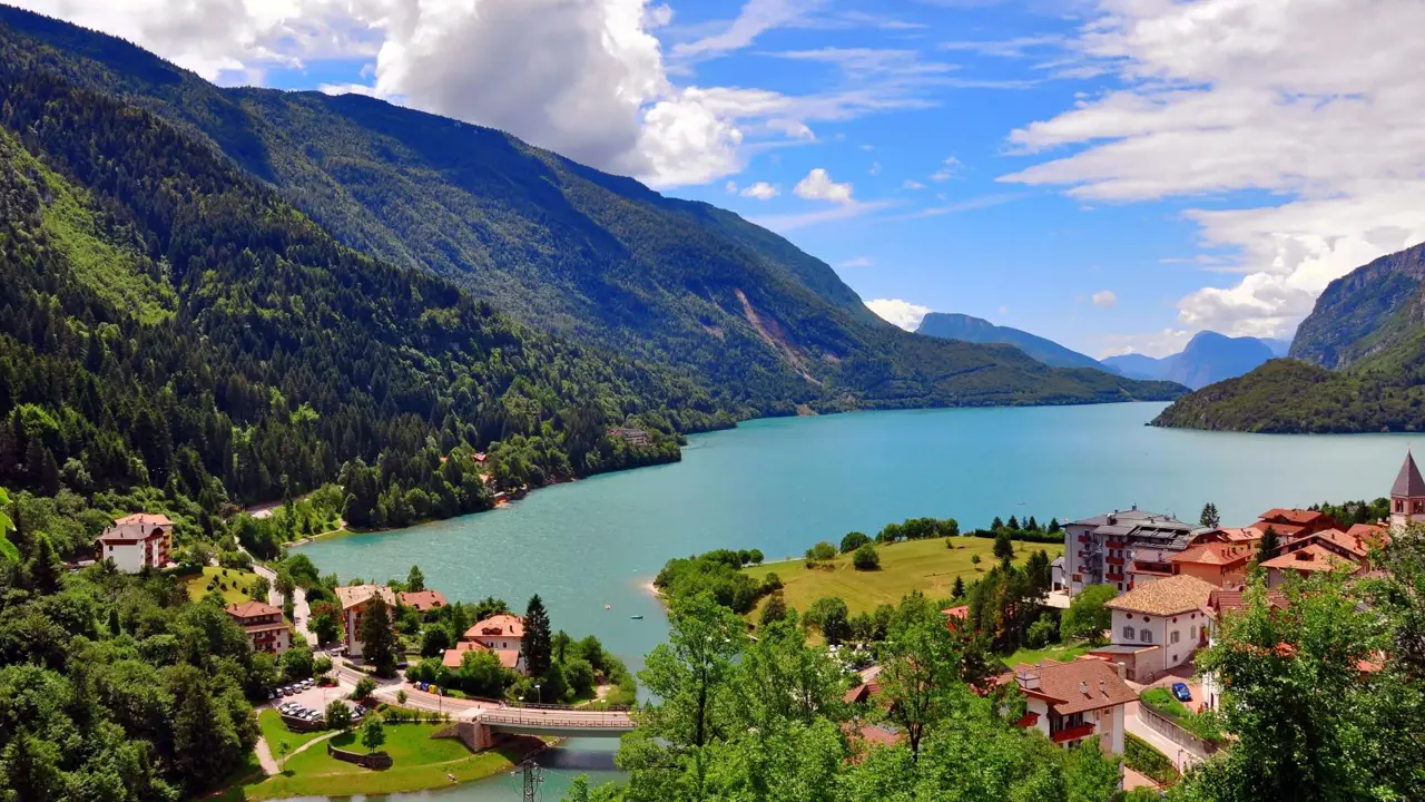 Molveno Lake in Italy, with colourful houses in the foreground and rolling hills alongside the lake