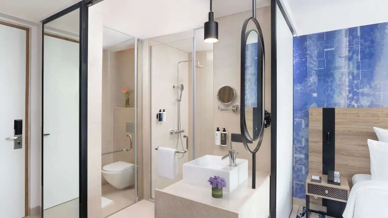 A bright modern bathroom at Novotel New Delhi City Centre with a glass shower, sink and toilet with beige décor