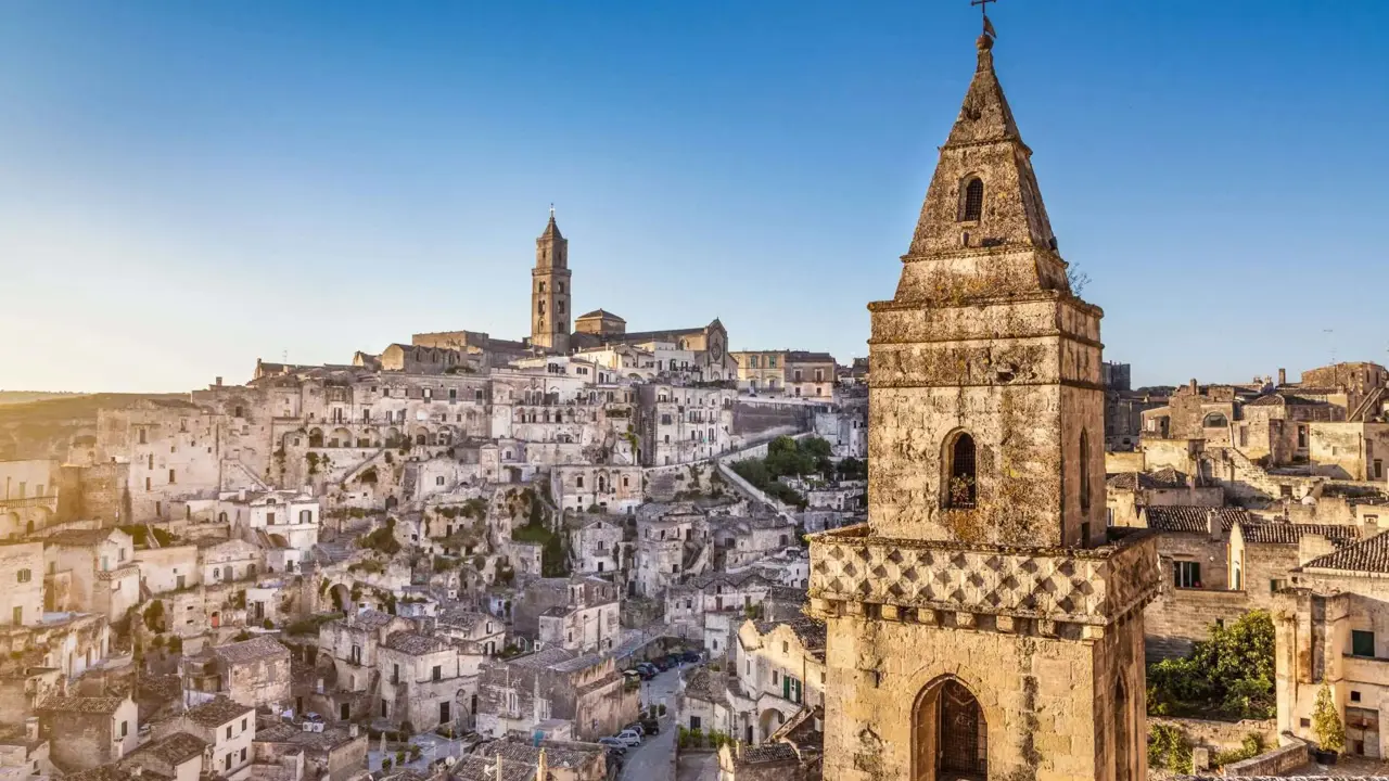 View of Matera’s ancient stone dwellings and rock-cut churches, with a bell tower overlooking the historic Sassi district under a clear blue sky