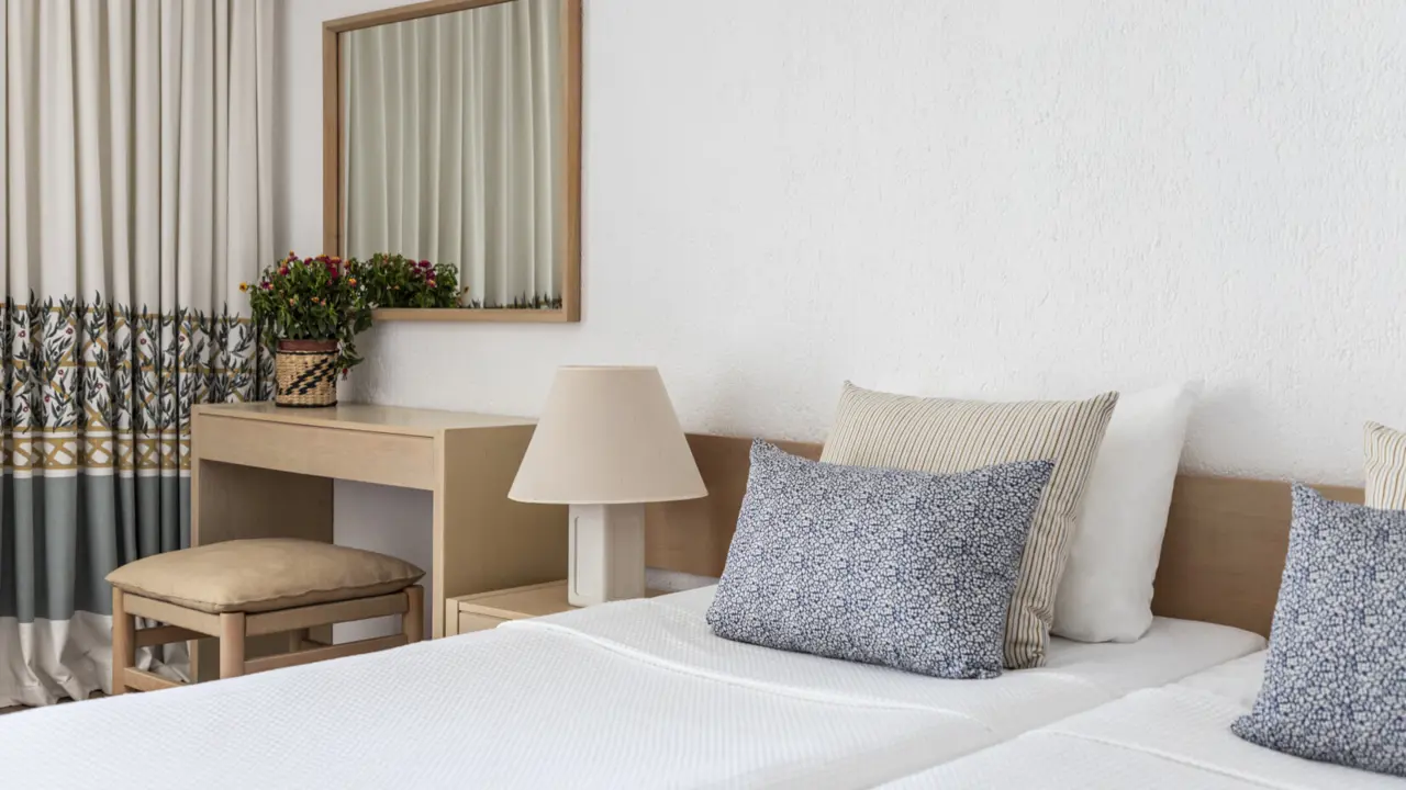 A twin room at Amalia Hotel, Olympia, featuring two twin beds with crisp white linens, wooden furnishings, and patterned curtains in neutral tones with dark green and gold accents
