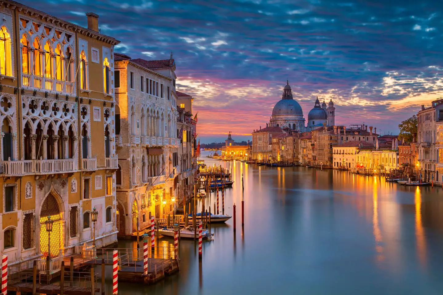 Sunset view of Venice featuring the iconic Salute Church beside a winding canal that stretches toward the open sea