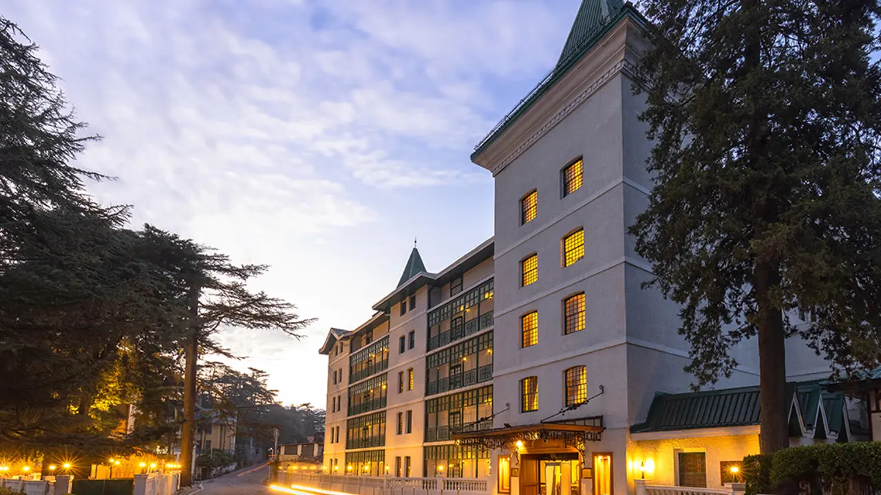 The Oberoi Cecil in Shimla at dusk, warmly illuminated, highlighting the hotel’s historic architecture and landscaped surroundings