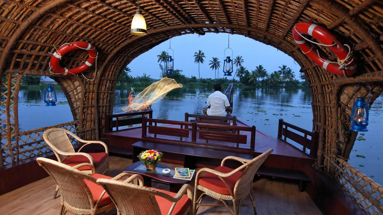View from the lounge area of a Kerala houseboat sailing on the river, showing calm waters, lush greenery, and palm trees along the banks