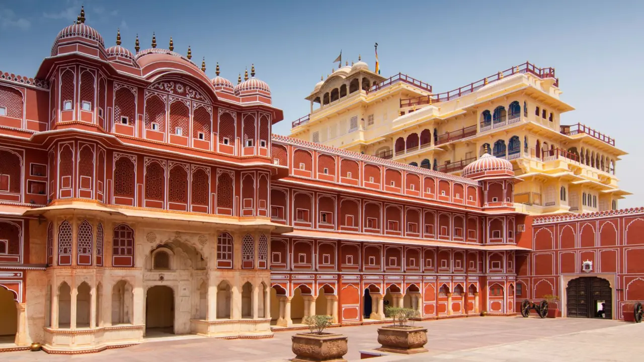 The ornate courtyard of the City Palace in Jaipur, displaying intricate red and white Rajasthani architecture with carved arches, domed roofs, and symmetrical windows