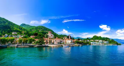 Lake Maggiore in Italy, with an Italian town on the shore beneath a bright, partly cloudy sky