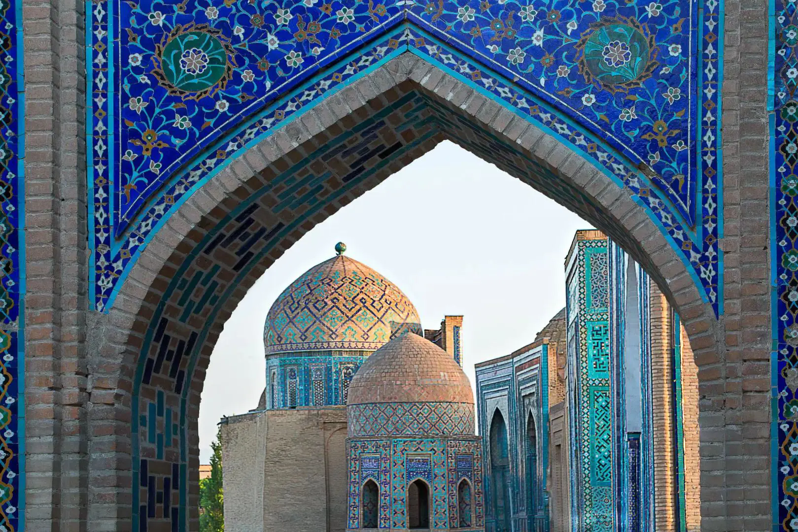 A tiled archway in Samarkand, Uzbekistan, framing a view of two domed temple roofs, each decorated with different intricate tile patterns