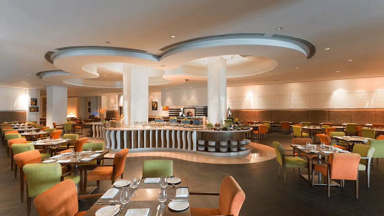 A spacious restaurant at WelcomHotel by ITC in Dwarka featuring colourful chairs, neatly set tables and a central buffet area