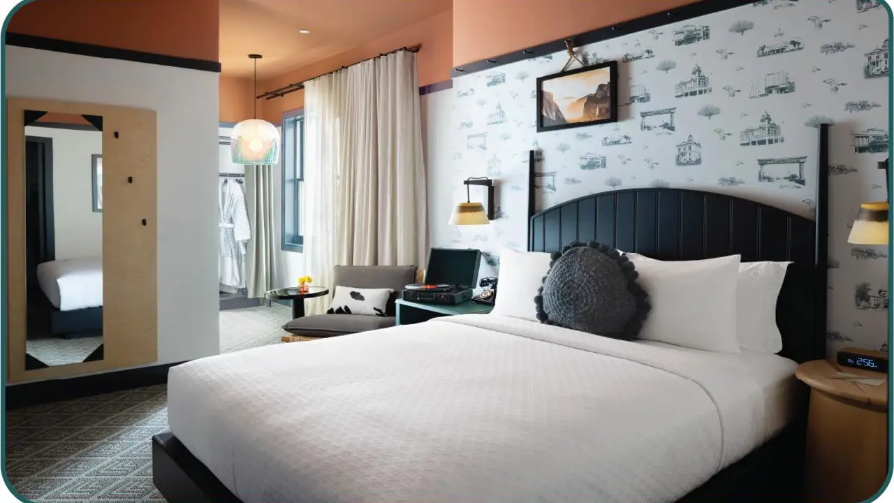 Stylish bedroom at the El Capitan Hotel, Merced, featuring a black wooden bed, patterned wallpaper behind, and orange-painted upper walls and ceiling, with warm lighting creating a cosy atmosphere