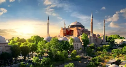 Hagia Sophia with its domes and minarets at sunset, surrounded by green trees in Istanbul
