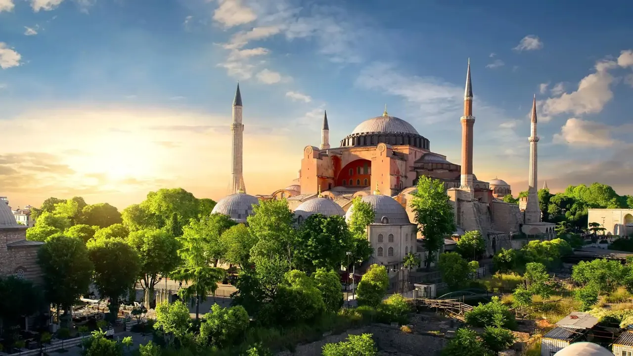 Hagia Sophia with its domes and minarets at sunset, surrounded by green trees in Istanbul