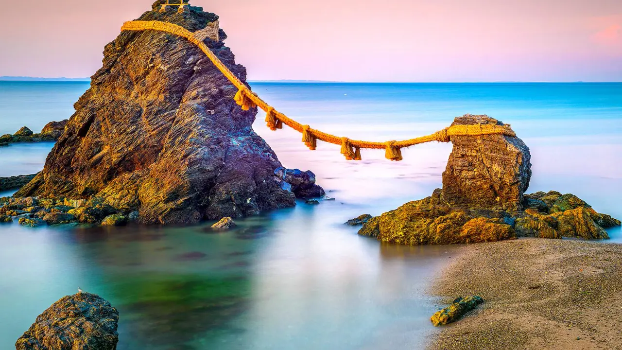 The Meoto Iwa Rocks, connected by a sacred rope in the sea at sunrise near Ise, Japan, with a small torii gate atop the larger rock