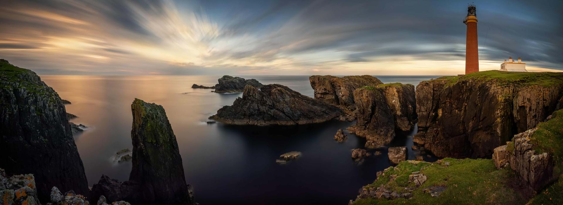 Long shot of the coast of the Isle of Lewis at sunset, showing the Butt of Lewis Lighthouse on the far right, looking out to sea