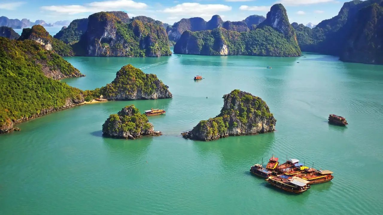 Traditional wooden boats sailing among limestone islands in Ha Long Bay, Vietnam