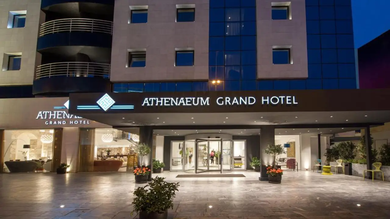 Front entrance of the Athenaeum Grand Hotel at night, with modern signage, glass doors, and potted plants