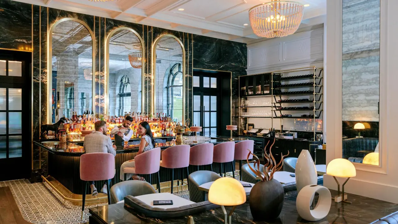 Stylish hotel bar at Fairmont Chateau with pink velvet stools, guests enjoying drinks, and a luxurious ambience