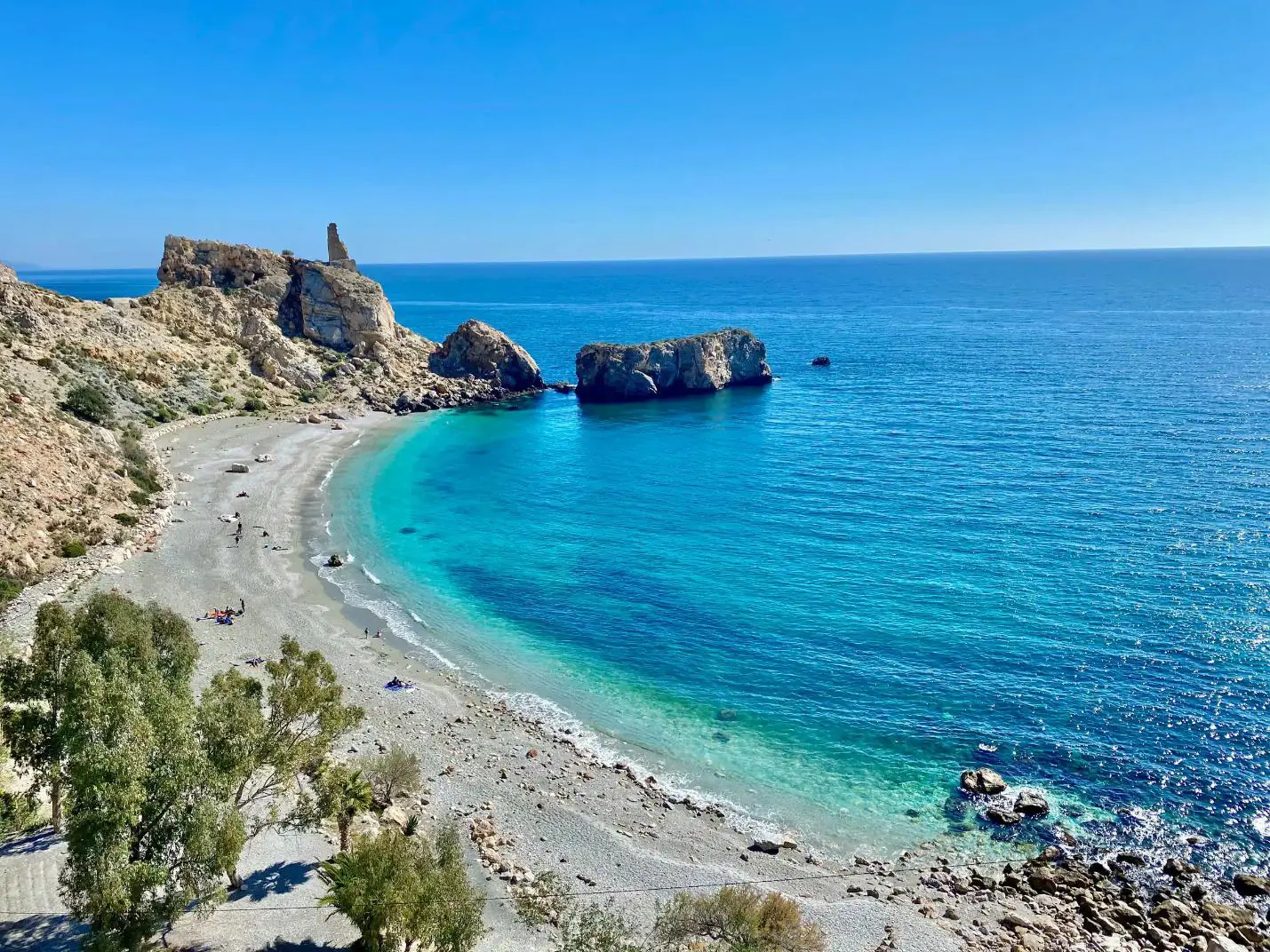 A wide sandy beach along the Costa de la Luz in Andalucía, Spain, with gentle waves lapping the shore under a clear blue sky