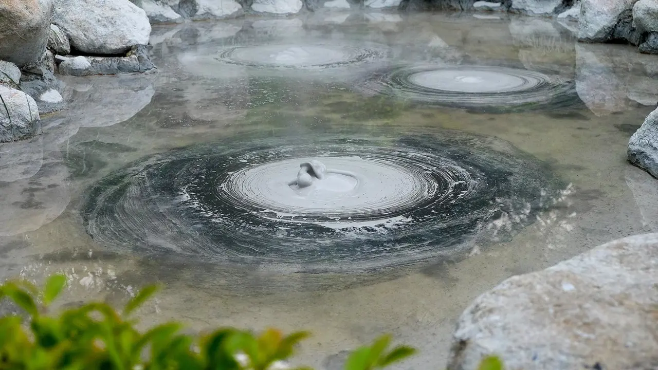 Bubbling grey mud pools in a steamy hot spring at the Mud Hell in Beppu, Japan, surrounded by rocks and greenery