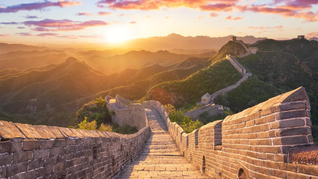 The Great Wall winding over mountain ridges, glowing in golden light at sunset, near Beijing, China