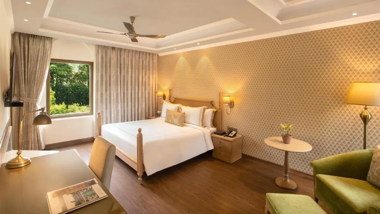 Bright hotel room at Heritage Village Resort And Spa in Gurugram, with a double bed, patterned wallpaper, desk and large window overlooking greenery