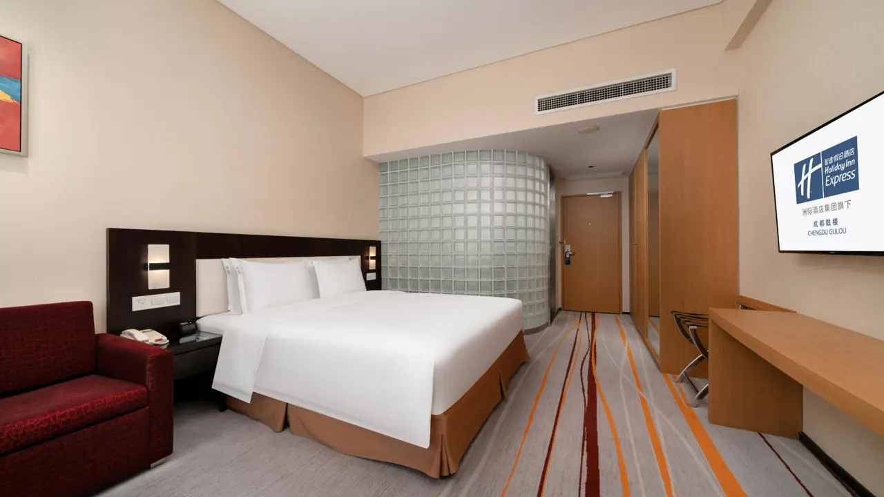 A bright and modern guest room at the Holiday Inn Express Gulou, featuring a comfortable double bed, a sleek desk area, and contemporary décor with warm wood tones and soft lighting