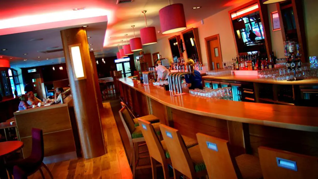 The Depot Bar at the Station House Hotel in Letterkenny, featuring a curved wooden bar, high stools, ambient red lighting, and cosy booth seating where guests are dining