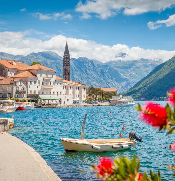 Scenic panorama view of the historic town of Perast at famous Bay of Kotor with blooming flowers on a beautiful sunny day with blue sky and clouds in summer, Montenegro, southern Europe