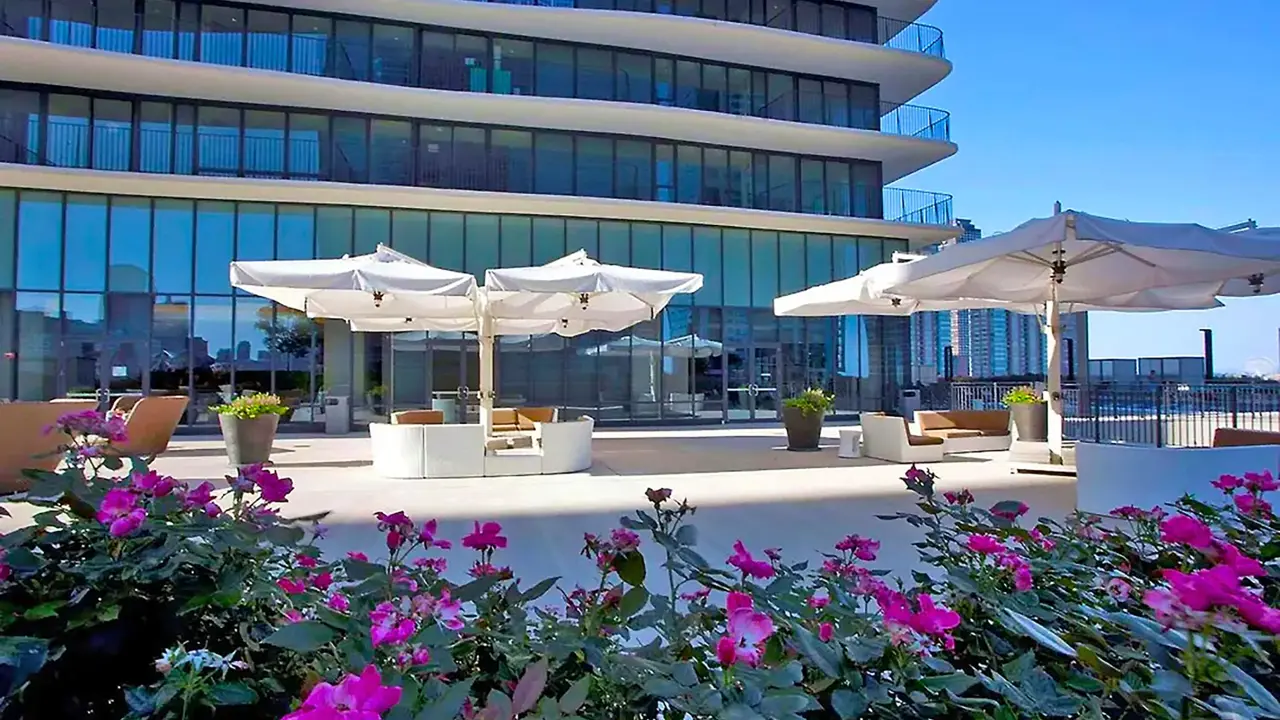 Modern terrace at Radisson Blu Aqua Hotel in Chicago, featuring lounge seating with umbrellas on the patio, and pink flowers and shrubs in the foreground