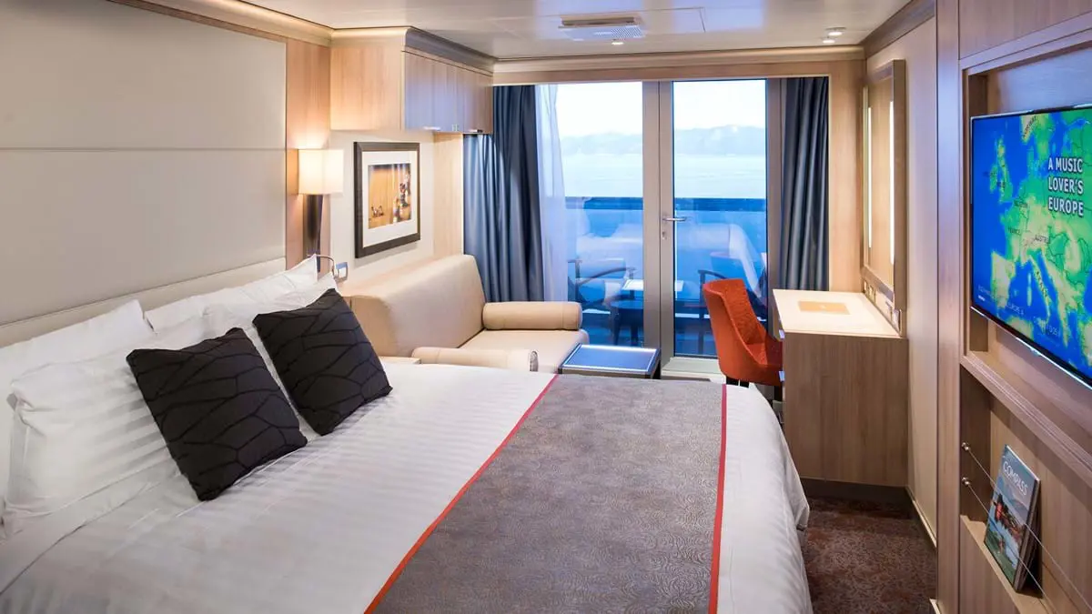 Interior of a double cabin on MS Koningsdam featuring a neatly made bed, modern decor, and a verandah with sliding glass doors overlooking the sea