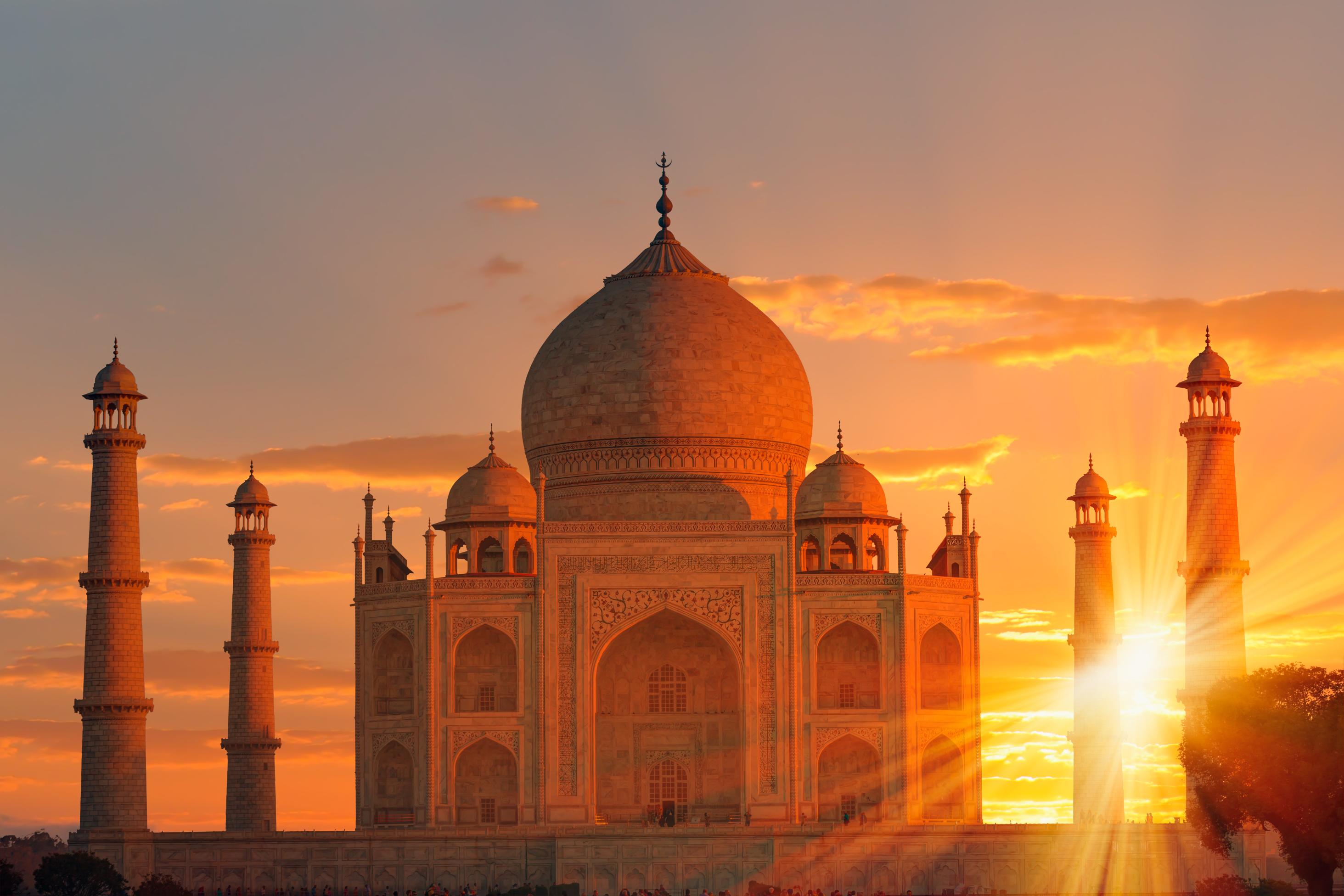 The Taj Mahal bathed in golden sunlight at sunset, with the sun setting between its elegant minarets, highlighting the detailed marble carvings and domed architecture