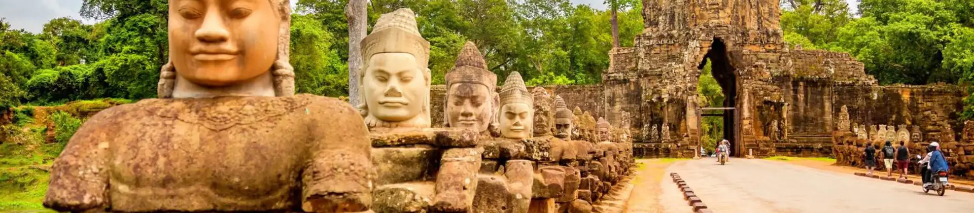 Stone statues line the entrance road to the majestic Angkor Thom gate, surrounded by dense green jungle