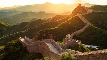 The Great Wall winding over green mountains at sunset, Beijing, China