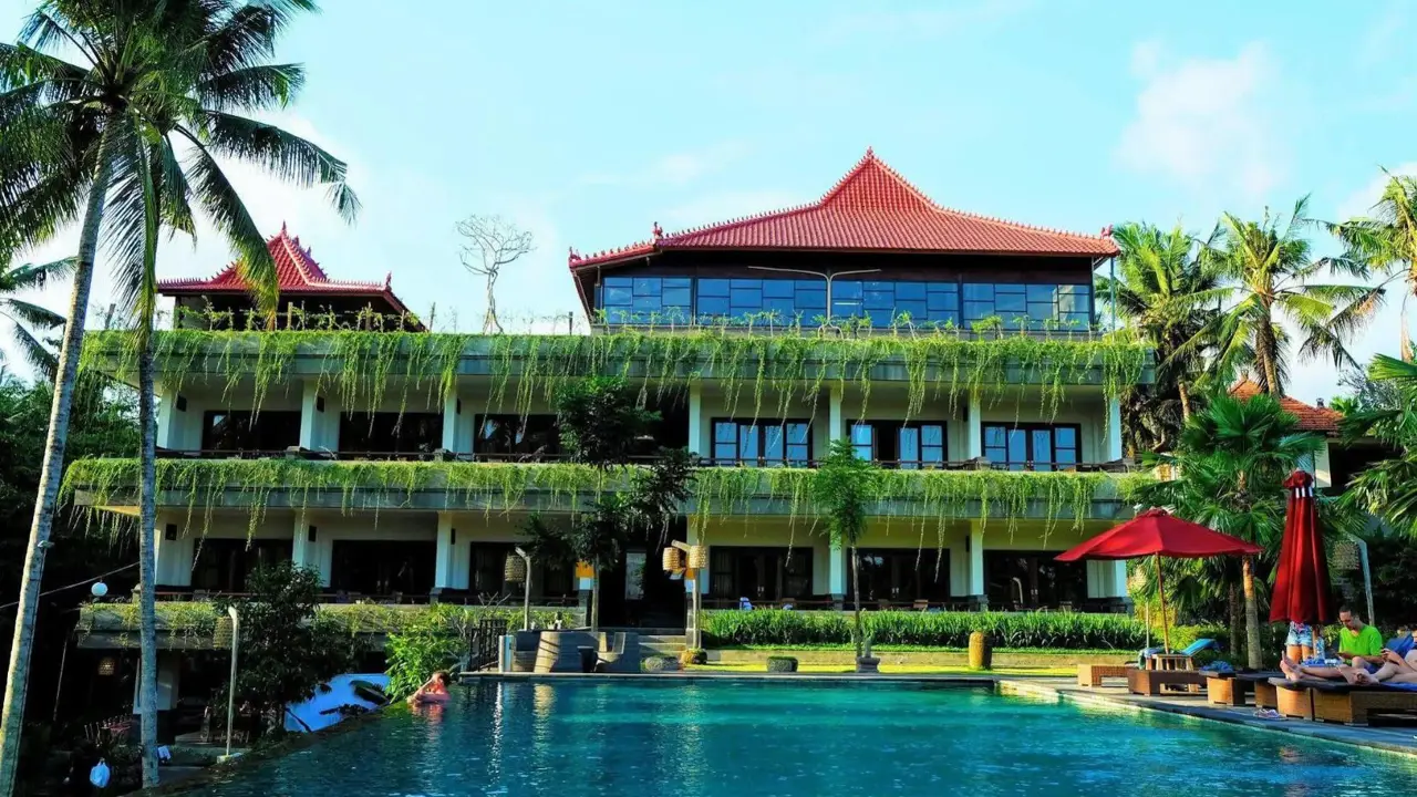 Exterior of Artini Dijiwa Hotel in Ubud, with balconies covered in greenery and a swimming pool in front, surrounded by palm trees