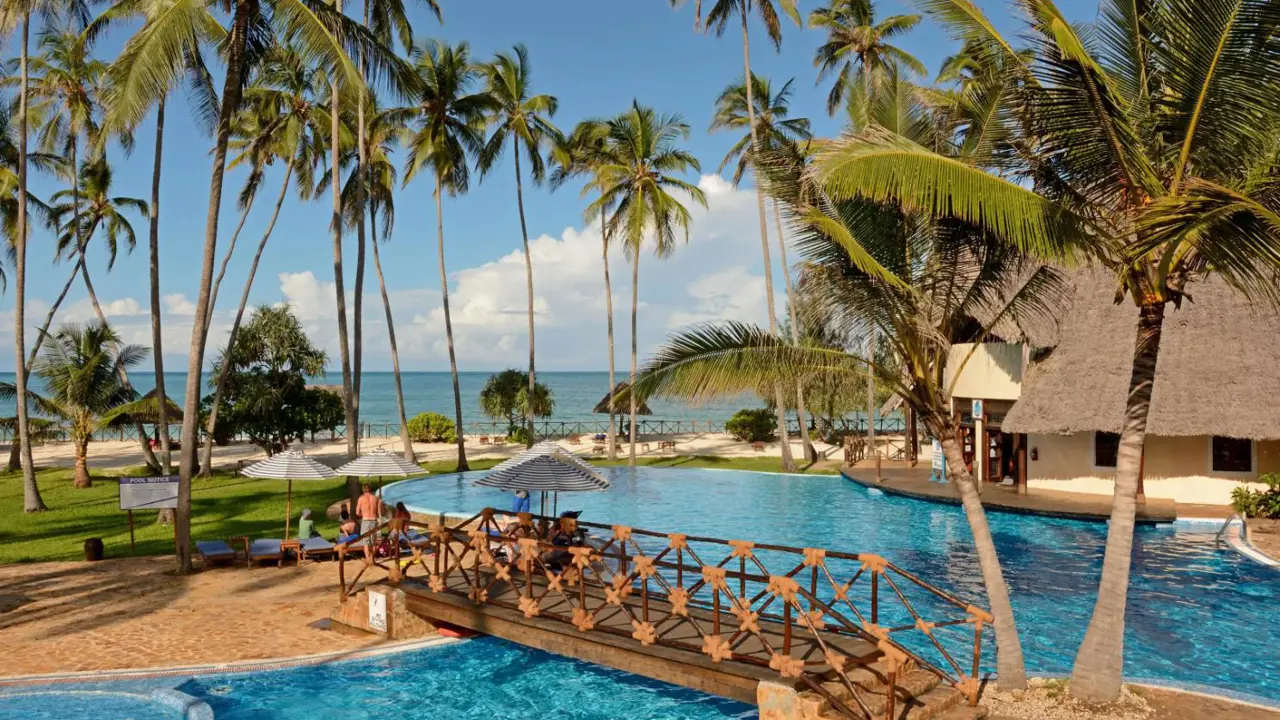 The pool area at Ocean Paradise Resort & Spa in Zanzibar, featuring a large, lagoon-style swimming pool surrounded by palm trees, sun loungers and thatched-roof buildings