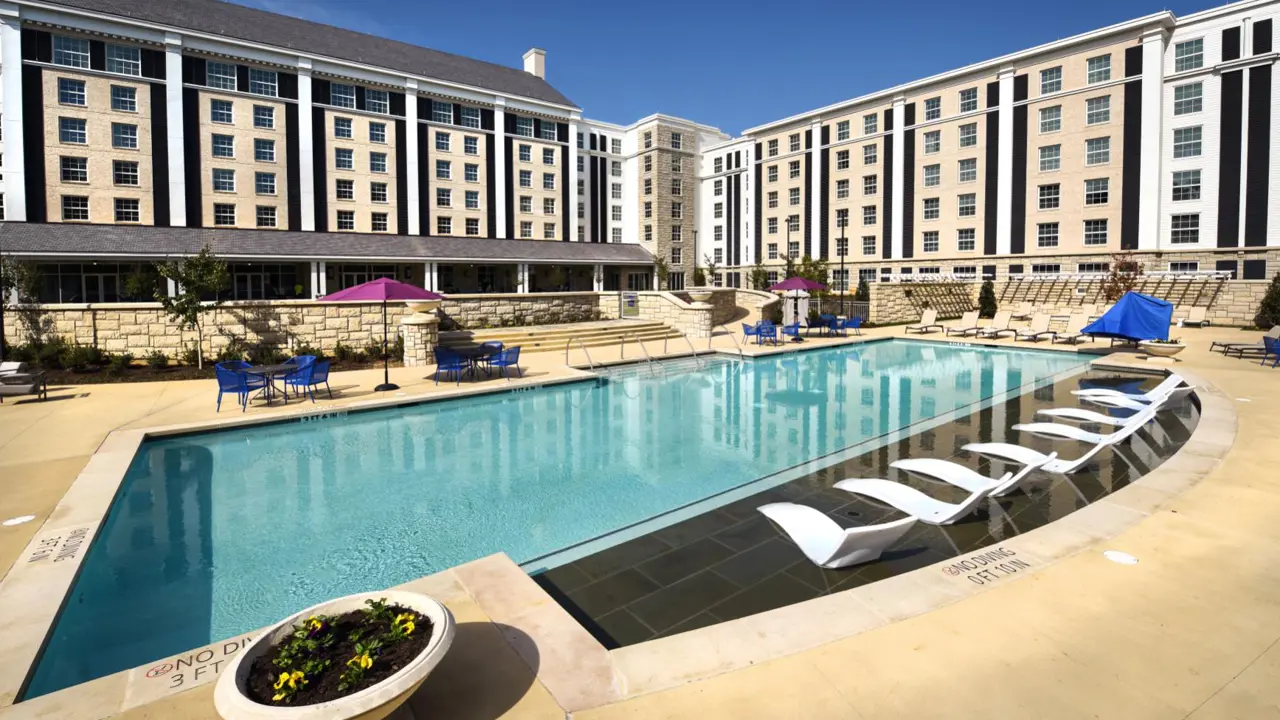 Outdoor pool at The Guest House at Graceland in Memphis, Tennessee, with in-water loungers, parasols, and the hotel’s brick building in the background under a clear sky