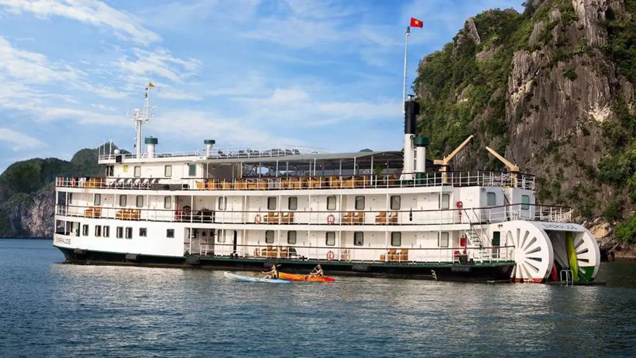The Emeraude Classic Cruise, a vintage-style white paddle steamer with green trim, anchored in the emerald waters of Ha Long Bay