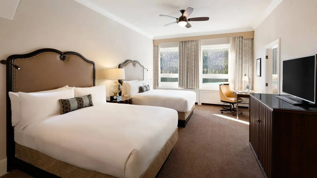 A twin room at Fairmont Chateau, Lake Louise in a warm modern style with two double beds and a mountain view