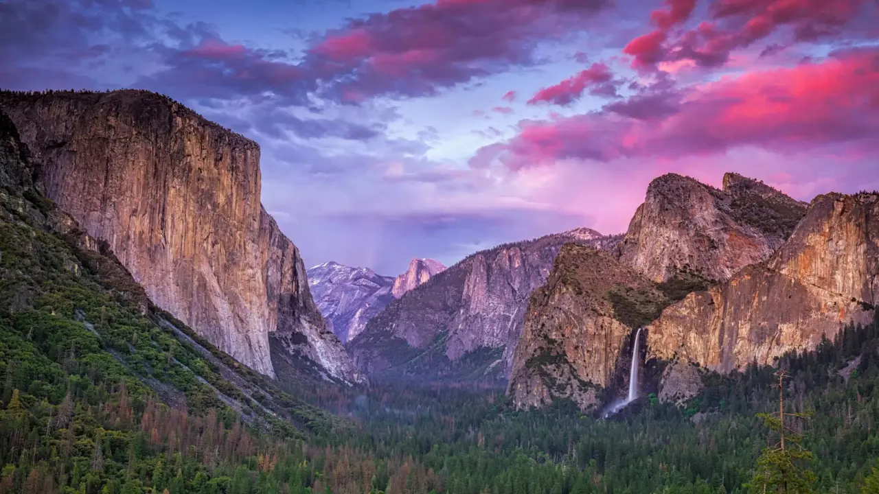 Breathtaking view of Yosemite National Park, California, featuring towering granite cliffs and lush green forests beneath a pink and blue sky at sunset
