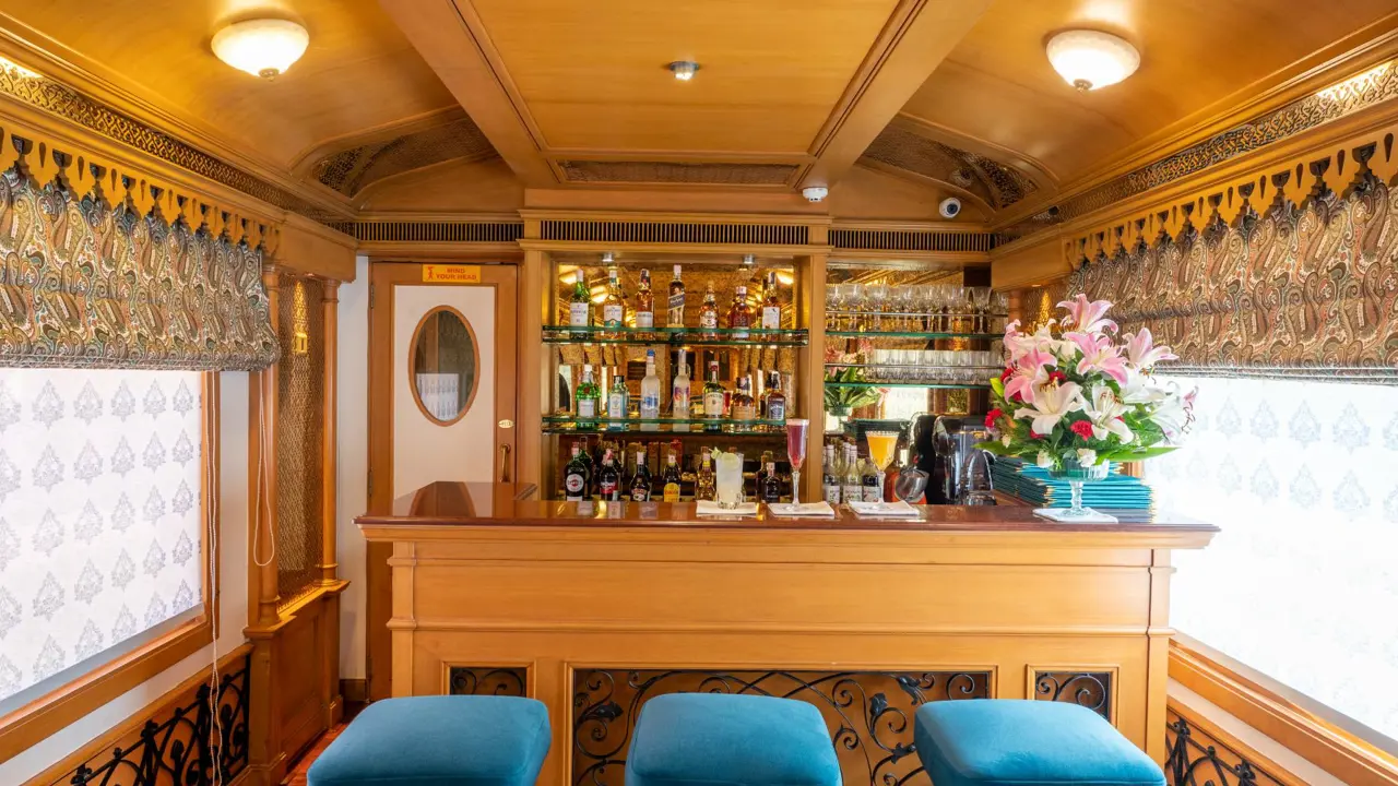 The Deccan Odyssey bar carriage with three teal bar stools, three drinks on the counter, and a range of bottles displayed behind the bar