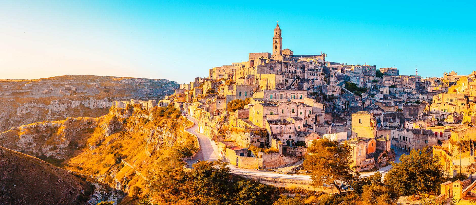 A panoramic view of the historic stone town of Matera, Italy, with ancient buildings stacked on a hillside in the golden glow of sunset