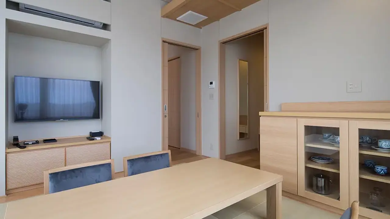 Stylish and spacious corner deluxe room in Hotel Kowakuen Haruka, with minimalist Japanese décor, featuring a low wooden table, tatami flooring, and display cabinets with tableware