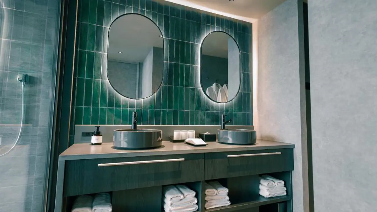 Modern bathoom at FAV LUX Nagasaki with double sinks, green tiled wall, round mirrors, and neatly arranged towels