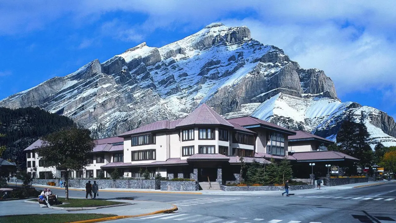 Elk + Avenue Hotel in Banff with a backdrop of rugged, snow-dusted mountains and a few pedestrians crossing the street